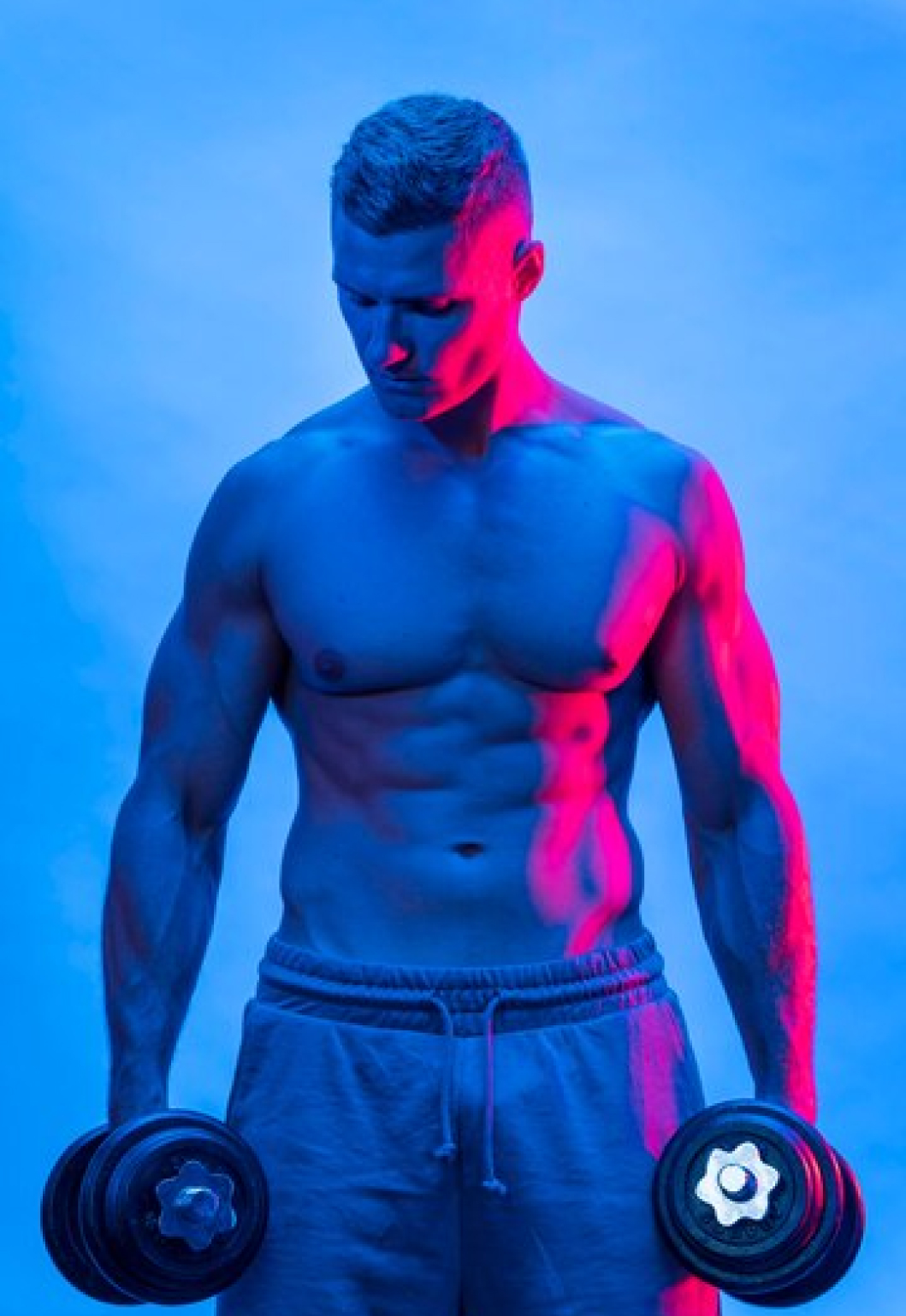 Спортивный мужчина в спортивных штанах держит в руках гантели